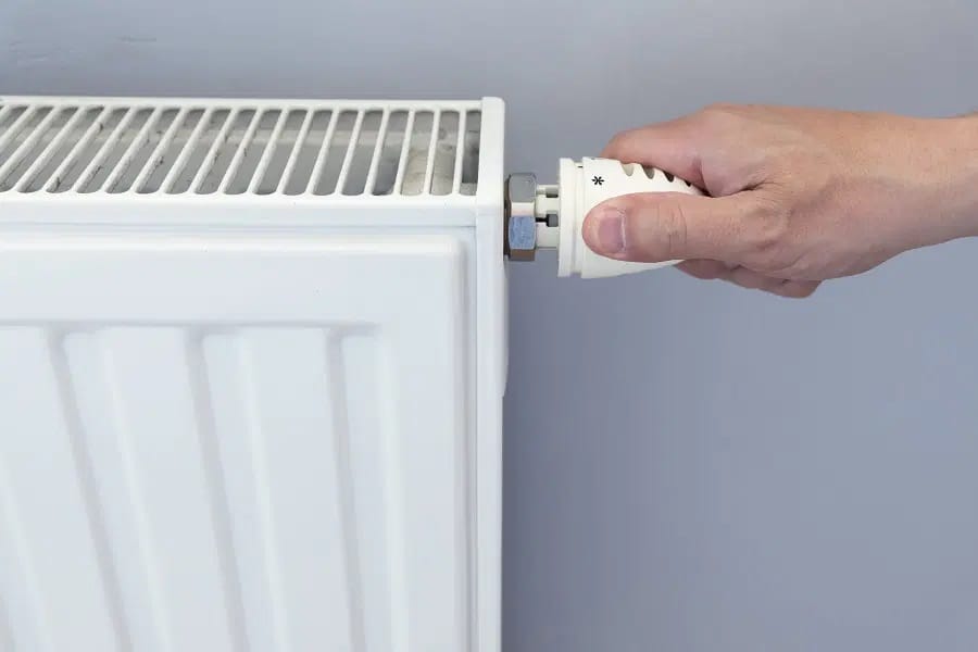 Main tenant la tête thermostatique d’un robinet de radiateur blanc