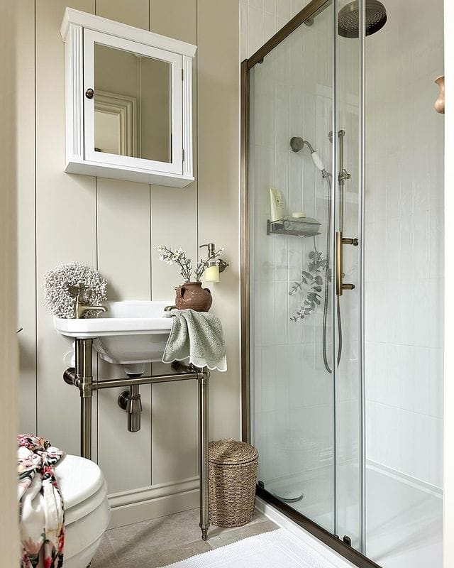 Salle de bain beige et blanche avec douche, lavabo et robinetterie à la finition or brossé