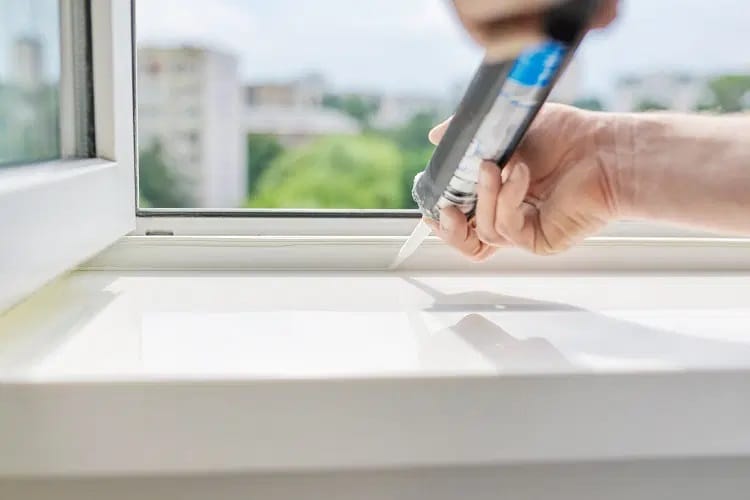 Homme étanchéifiant une fenêtre de salle de bain pour garder la chaleur à l’intérieur