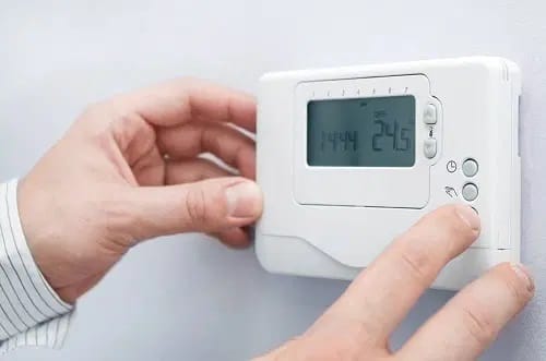 Personne éteignant le chauffage au thermostat pour préparer la purge du radiateur