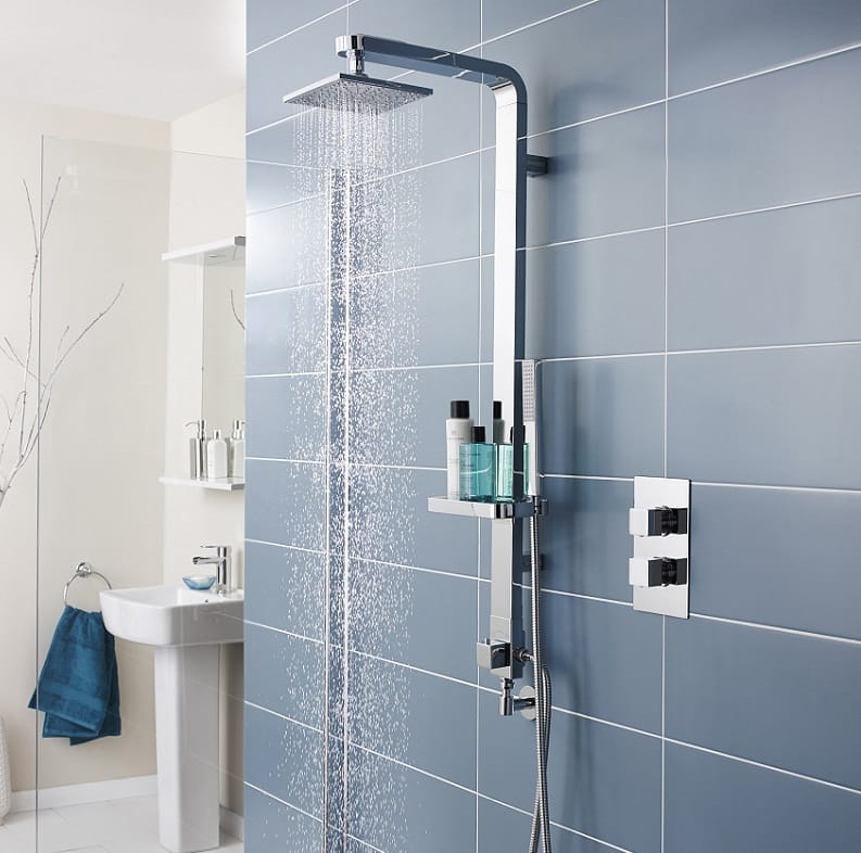 Colonne de douche chromée avec tomber de l’eau en pluie sur un mur carrelé bleu gris