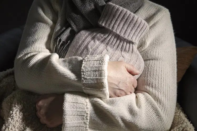 Femme portant une écharpe sous et sous une couverture tenant contre elle une bouillotte