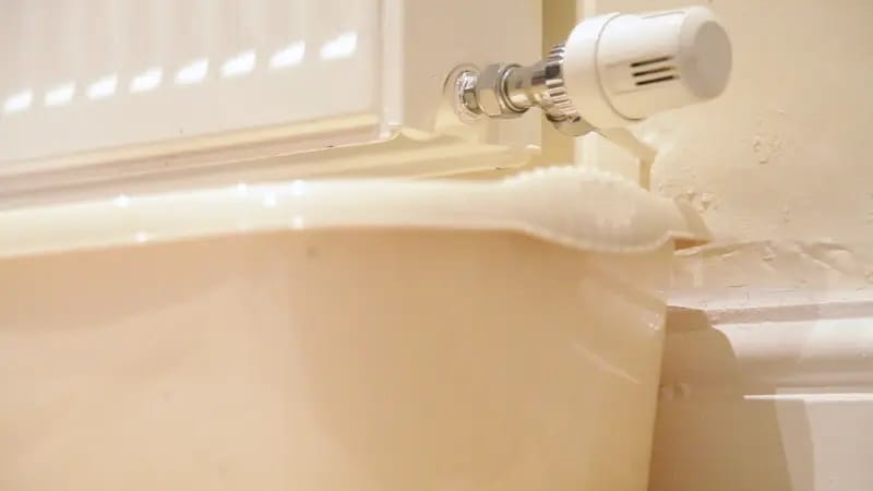 Grande bassine placée sous le robinet thermostatique d’un radiateur blanc