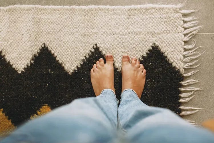 Pieds de femme se tenant sur un tapis posé sur un sol en carrelage