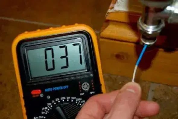 Personne tenant un thermomètre affichant 037° au niveau de la tuyauterie du radiateur
