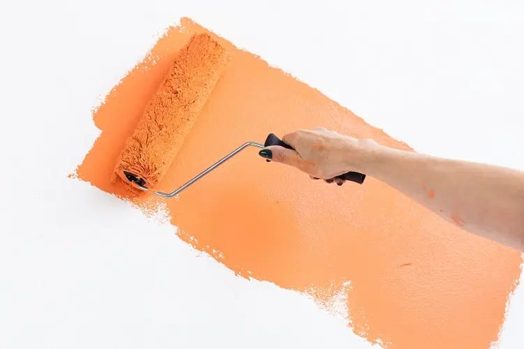 Femme tenant un rouleau de peinture couvert d’une couleur orangée peignant le mur blanc