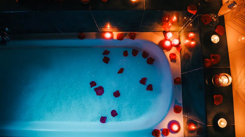 Vue du dessus d’un bain moussant rempli de pétales de roses rouges éclairé à la bougie