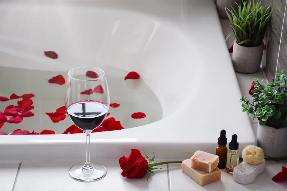 Verre de vin rouge sur le rebord d’une baignoire remplie d’eau et de pétales de rose rouge